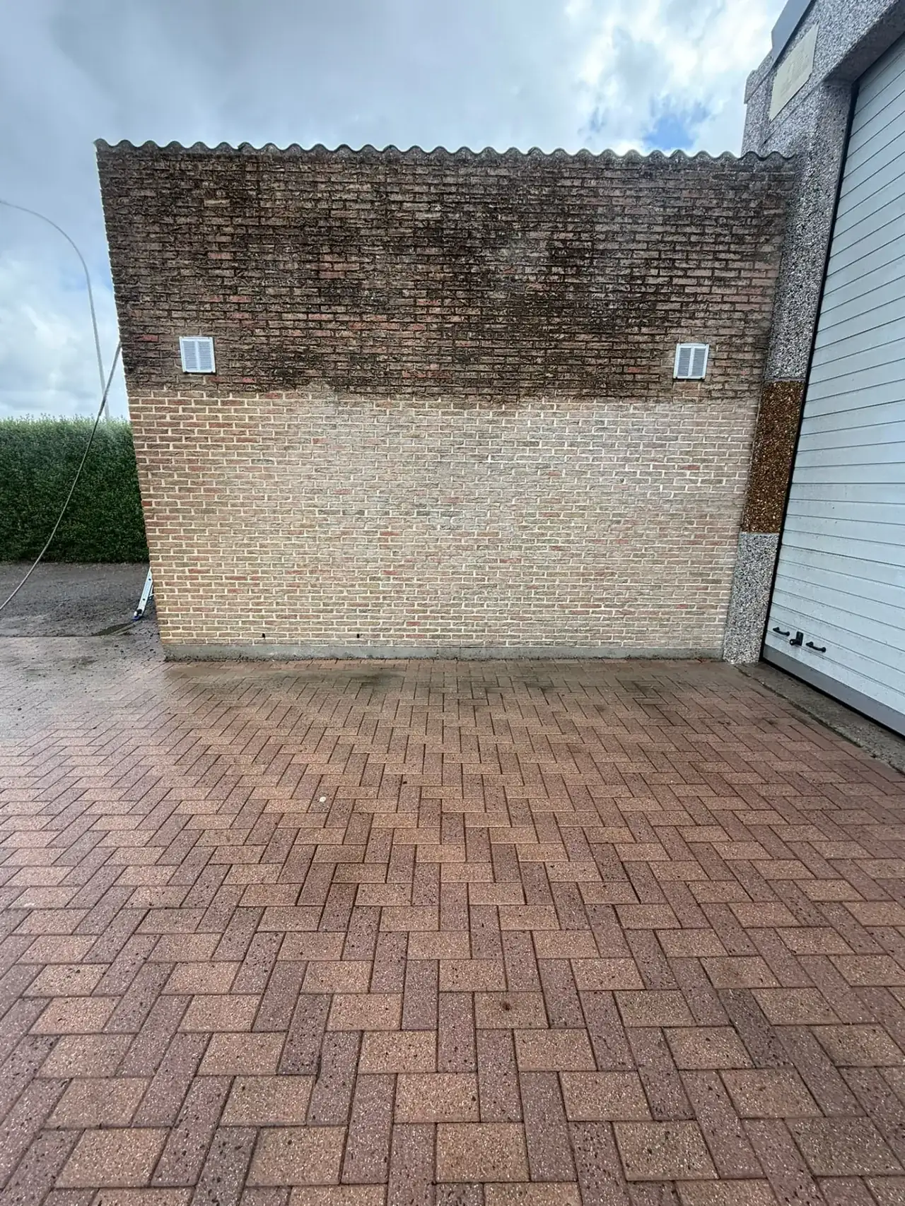 Bakstenen gevel tijdens de reiniging: bovenaan vervuild, onderaan proper