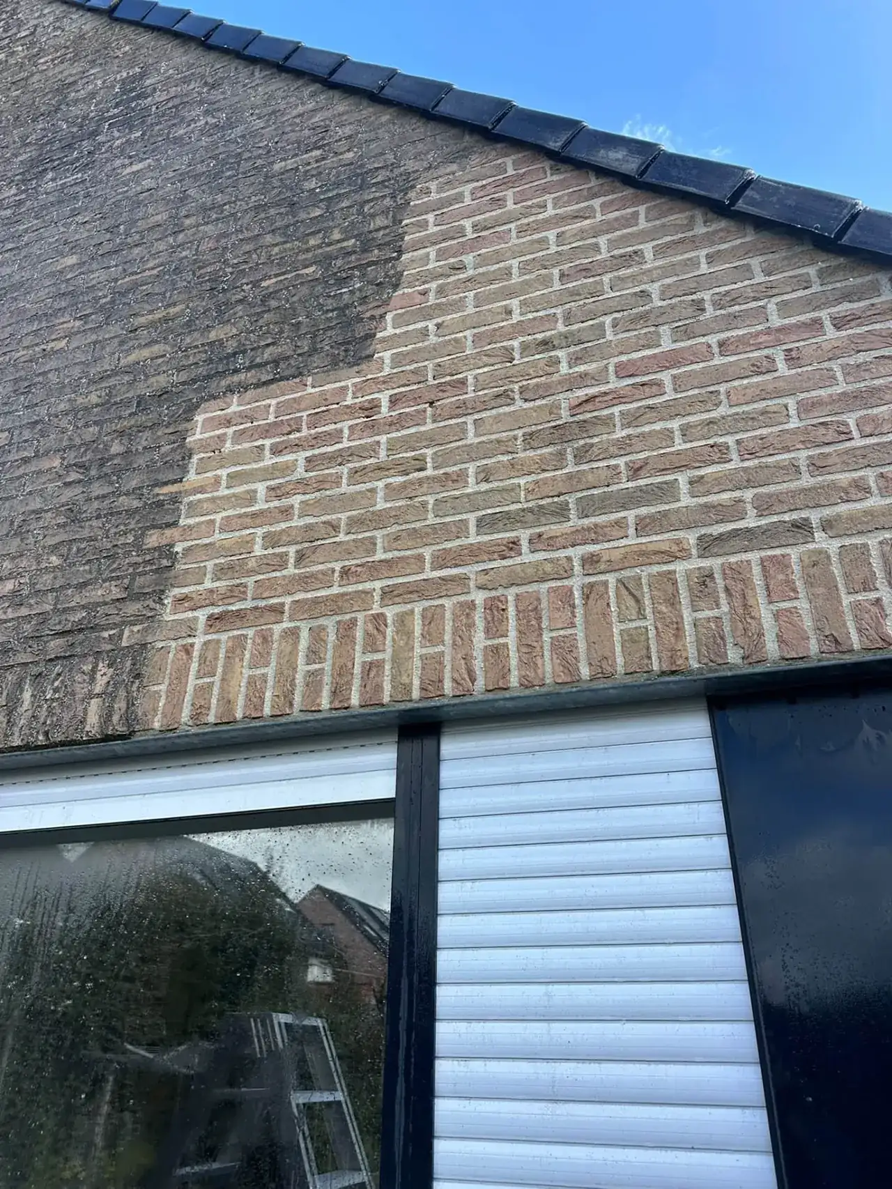 Bakstenen puntgevel tijdens de reiniging: links vervuild, rechts gereinigd